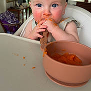 Jack is registered to the contest to win money with this photo: baby, blue_eyes, high_chair, orange_food, spoon, messy_face, feeding_time, indoor, child, infant, kitchen, table, food, meal, cute, young_child, person, face, hands, bright_light