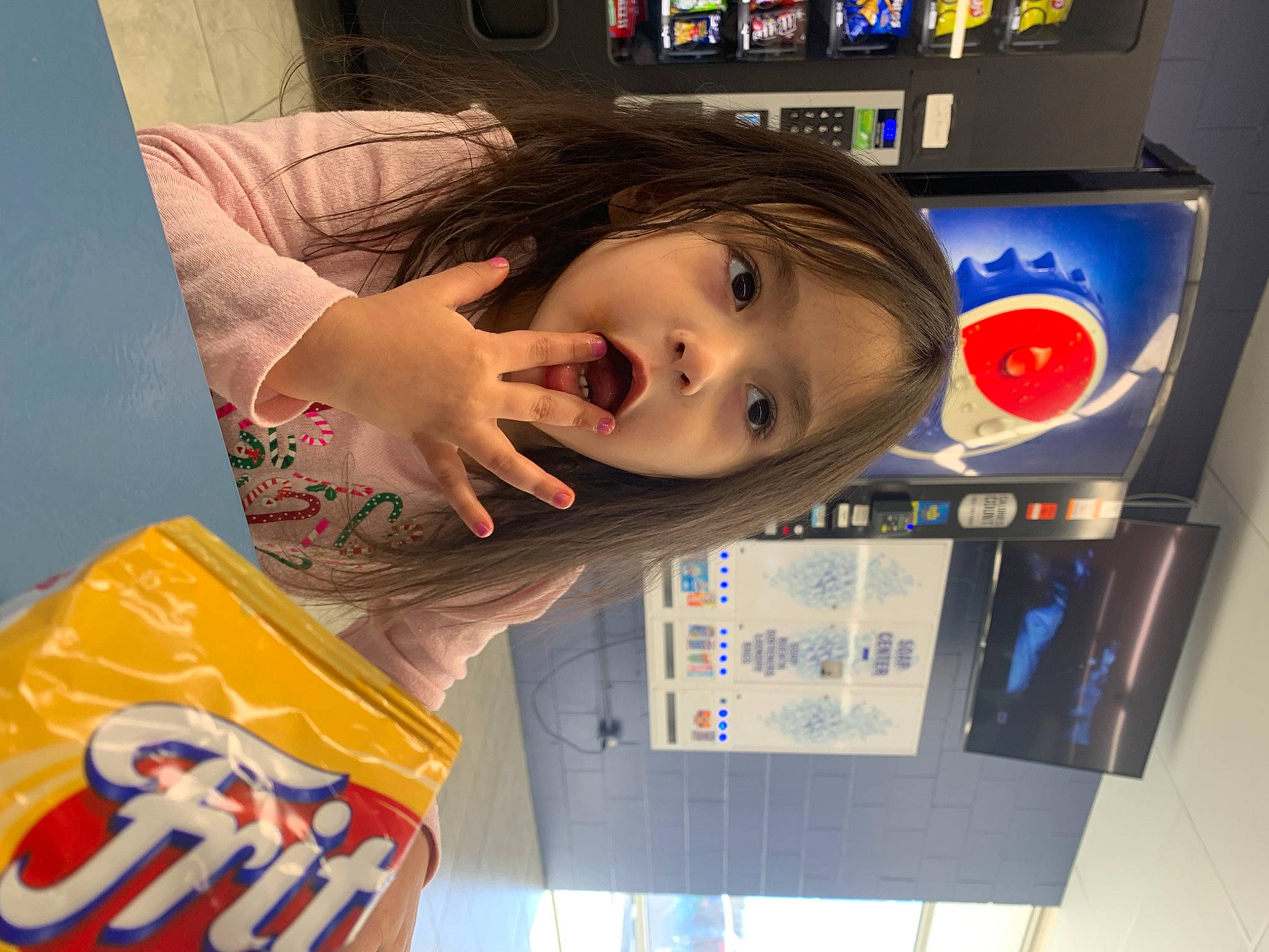 Liliana is registered to the contest to win money with this photo: child, elbow, eyelash, finger, fun, gesture, happy, logo, machine, nose, person, room, sleeve, t_shirt, thumb, toddler