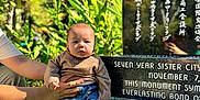 Elmer is registered to the contest to win money with this photo: baby, child, person, sitting, outdoor, greenery, plants, rock, monument, text, sweater, jeans, shoes, hands, support, daylight, nature, portrait, casual_clothing, expression