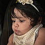 baby, child, headband, flower, curly_hair, closeup, face, expression, bib, infant, skin, portrait, cute, young_child, dark_background, soft_lighting, looking_down, indoor, adorable, focused