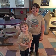 Robert Kenneson Ii is registered to the contest to win money with this photo: child, children, smiling, tshirt, dinosaur, bowling_alley, bowling_ball, floor, indoor, person, young, casual_clothing, shoes, happy, standing, recreation, leisure, fun, siblings, portrait