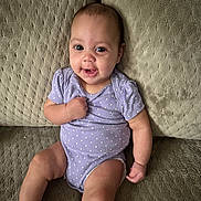 Araceli is registered to the contest to win money with this photo: baby, infant, smiling, purple_onesie, polka_dot, couch, textured_fabric, sitting, happy, child, skin, face, arm, leg, furniture, indoor, cute, portrait, young_child, comfortable
