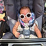 baby, sunglasses, stroller, child, seatbelt, flower_pattern, clothing, infant, outdoor, person, cute, fashion, summer, accessory, headwear, portrait, sitting, small_child, baby_girl, sunlight