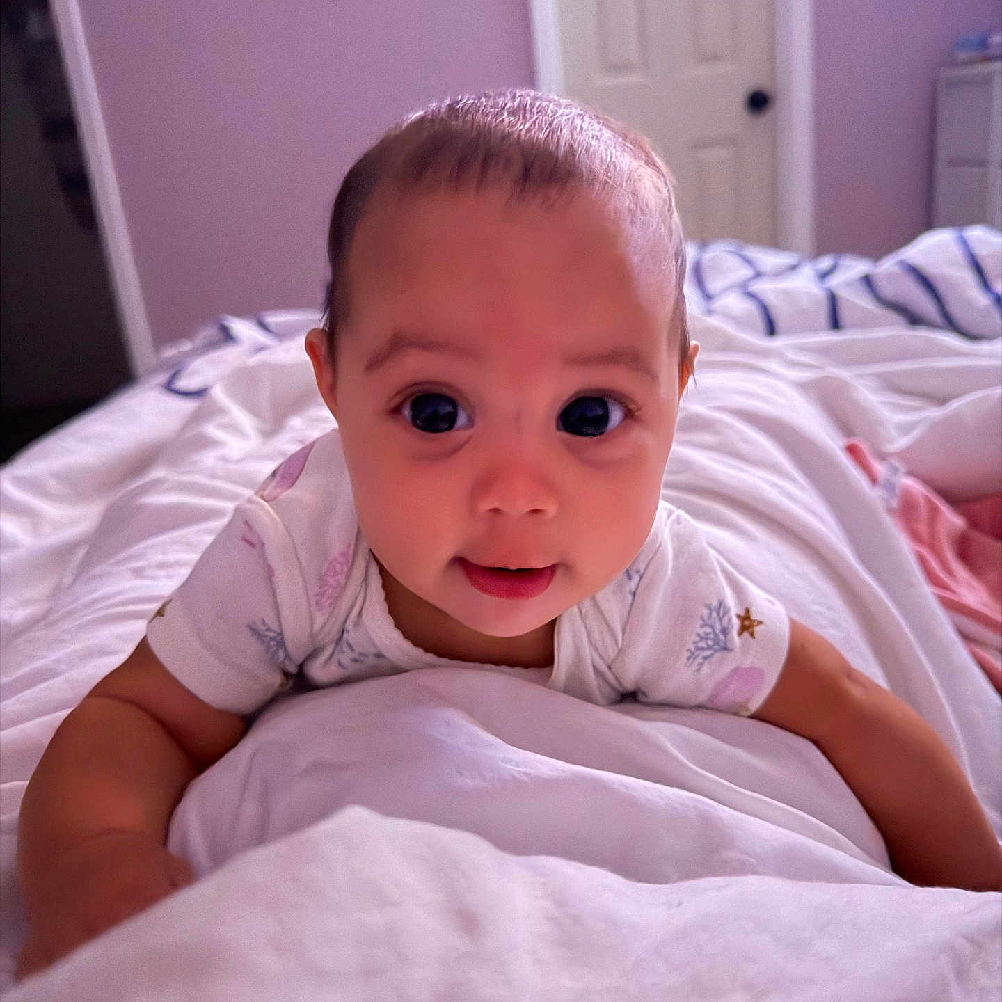 Araceli is registered to the contest to win money with this photo: baby, infant, bed, blanket, white, room, door, curious, wide_eyes, smile, crawling, clothing, short_sleeve, indoor, soft_light, pastel_walls, furniture, head, person, portrait
