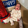 Araceli is registered to the contest to win money with this photo: baby, infant, pajamas, bear_pattern, couch, beige, gnome, red_hat, decorative_pillow, happy, smiling, seated, indoor, cute, plush, child, home, cozy, portrait, furniture