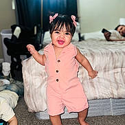 Kalye is registered to the contest to win money with this photo: bed, bedroom, bows, carpet, child, child_playing, cute, family, furniture, hair_bangs, happy, home, indoor, lamp, person, phone, pink_romper, smiling, standing, toddler
