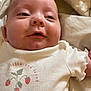 Isolde is registered to the contest to win money with this photo: baby, infant, close_up, smiling, cute, white_shirt, strawberry_design, text_on_clothing, blanket, soft, lying_down, happy, face, skin, eyes, mouth, tiny_hand, child, adorable, portrait