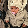 baby, child, pacifier, hat, knit_hat, coat, winter_clothing, stroller, hand, holding_hand, blue_eyes, cute, infant, bundle_up, warm_clothing, button, fabric, portrait, seated, outdoor