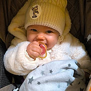 Emma a rejoint le concours — aidez-le/la à gagner de superbes lots ! baby, pacifier, knit_hat, bambi_patch, blanket, star_pattern, fluffy_jacket, smiling, cute, child, infant, cozy, warm_clothing, indoors, portrait, close_up, hand, face, blue_eyes, happy