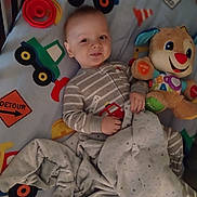 Zayden joined the competition — help win amazing prizes! baby, bed, blanket, child, colorful, comfort, cute, expression, fabric, face, hand, indoor, lying_down, pajamas, playful, smile, soft, stuffed_animal, toy, young
