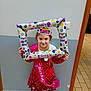 birthday, celebration, child, colorful, dress, floor_tiles, girl, happy, holding, indoor, inflatable_frame, party, person, pink_shoes, polka_dots, sash, smile, tiara, wall, young