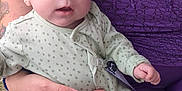 Oakley is registered to the contest to win money with this photo: baby, infant, adult, holding, onesie, purple_clothing, polka_dot, blue_eyes, hand, outdoor, gravel, tattoo, ring, close_up, face, skin, person, sitting, gentle, caring