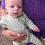 baby, infant, adult, holding, onesie, purple_clothing, polka_dot, blue_eyes, hand, outdoor, gravel, tattoo, ring, close_up, face, skin, person, sitting, gentle, caring