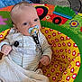 Oakley is registered to the contest to win money with this photo: baby, pacifier, striped_onesie, baby_seat, colorful, flower_pattern, blanket, blue_eyes, infant, comfort, indoor, child, cute, clothing, furniture, soft_toys, young_child, hand, face, person