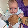 baby, infant, person, adult, hand, tattoo, watch, clothing, white_onesie, blue_eyes, face, indoor, portrait, holding, sitting, furniture, purple_shirt, skin, expression, home