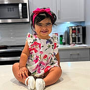 Amely joined the competition — help win amazing prizes! toddler, child, smiling, headband, pink, dress, floral, kitchen, counter, appliances, microwave, cabinets, modern, happy, sitting, white_shoes, indoors, person, cute, portrait