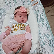 Harper is registered to the contest to win money with this photo: baby, infant, headband, flower, shirt, text, pink, white, cushion, seat, pattern, floor, tile, clothing, socks, newborn, resting, indoors, person, cute