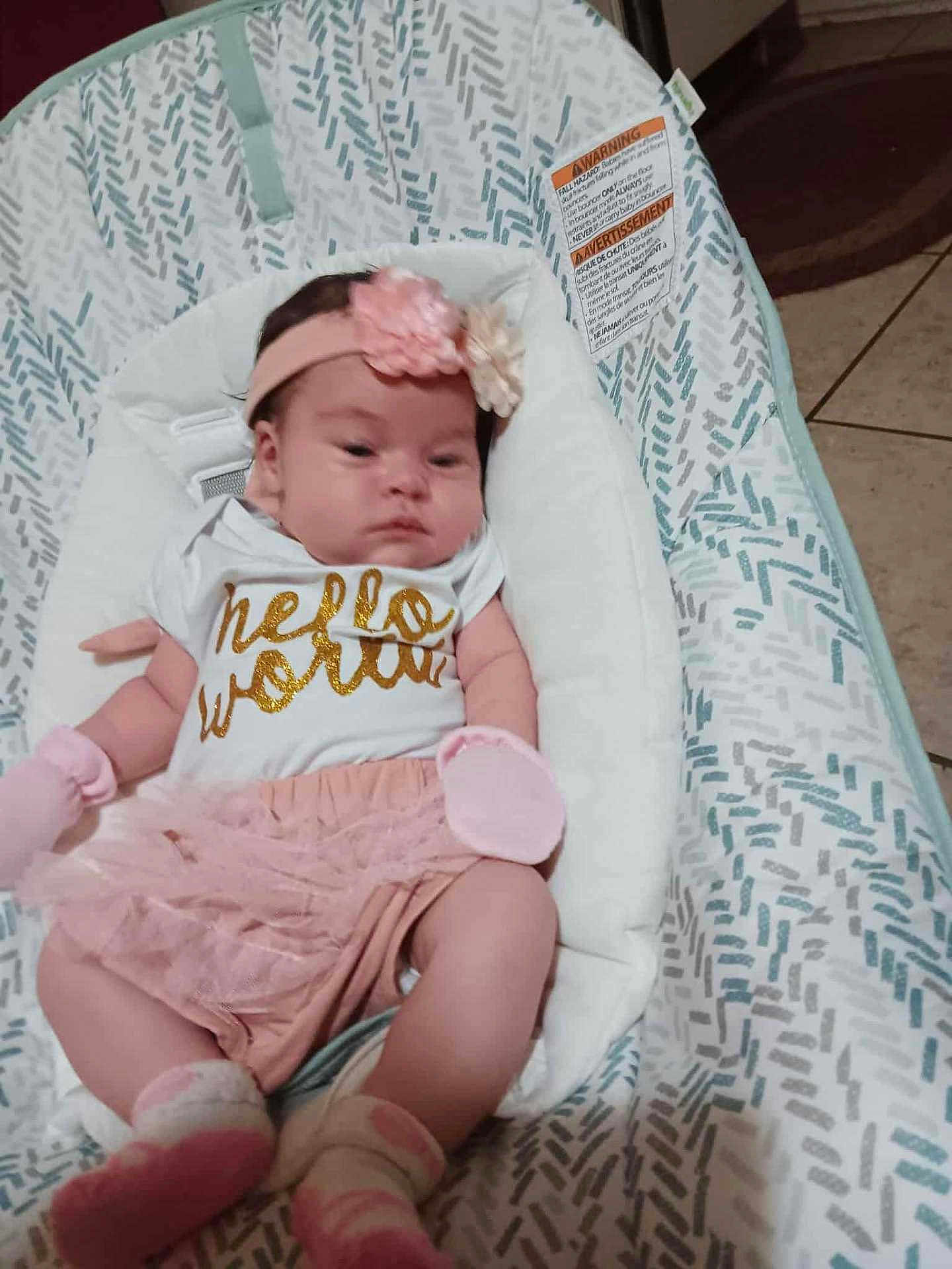 Harper is registered to the contest to win money with this photo: baby, infant, headband, flower, shirt, text, pink, white, cushion, seat, pattern, floor, tile, clothing, socks, newborn, resting, indoors, person, cute