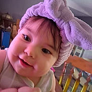 Harper is registered to the contest to win money with this photo: baby, bunny_ears, child, closeup, curly_hair, cute, face, furniture, happy, headband, headwear, indoor, infant, person, playful, portrait, purple, smiling, soft_texture, wooden_chair