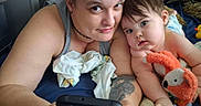 Harper is registered to the contest to win money with this photo: woman, baby, child, plush_toy, bed, blanket, tattoo, phone, smile, indoor, portrait, person, cushion, skin, casual, home, relaxation, closeup, expression, family