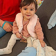 Athénaïs a rejoint le concours — aidez-le/la à gagner de superbes lots ! toddler, child, baby, girl, couch, blanket, pacifier, headband, pink_clothing, white_tights, person, indoor, seated, smiling, cute, cozy, soft_toys, adult_hand, casual_wear, home