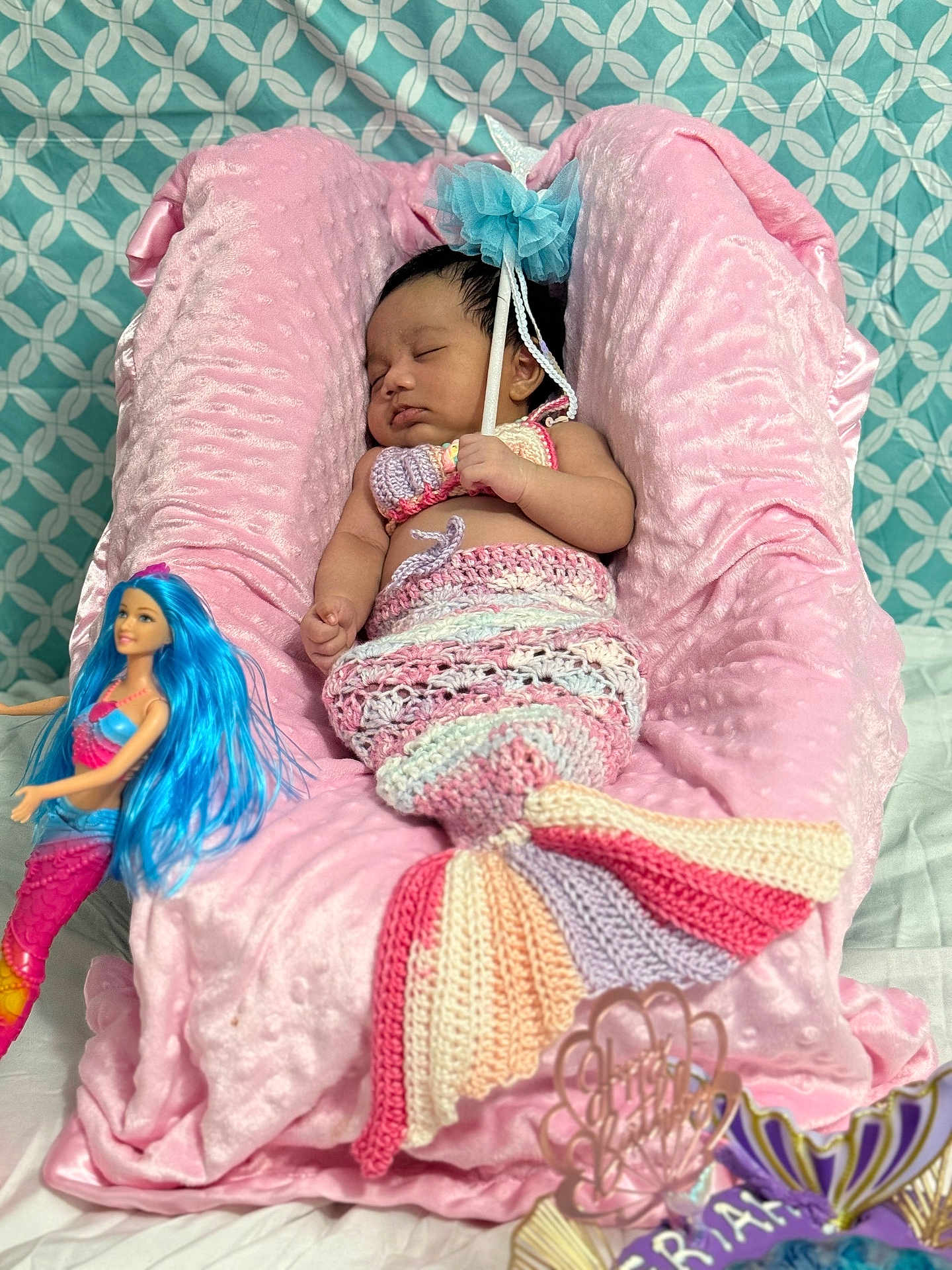 Severena is registered to the contest to win money with this photo: baby, sleeping, mermaid_costume, crochet, pink, plush, cushion, doll, toy, blue_hair, wand, patterned_background, fabric, bed, child, infant, cute, soft_texture, decor, resting