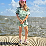 Rayne is registered to the contest to win money with this photo: child, girl, pink_cap, smile, green_outfit, shorts, sneakers, socks, dock, water, sky, clouds, sunny, outdoor, standing, portrait, daylight, happy, fashion, casual