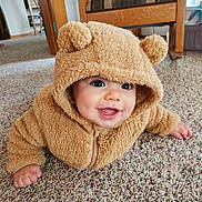 Liam is registered to the contest to win money with this photo: baby, infant, child, teddy_bear_hood, hooded_jacket, fuzzy_coat, carpet, smile, drooling, cute, indoors, portrait, close_up, big_eyes, chubby_cheeks, plush, zipped_jacket, hand, floor, home