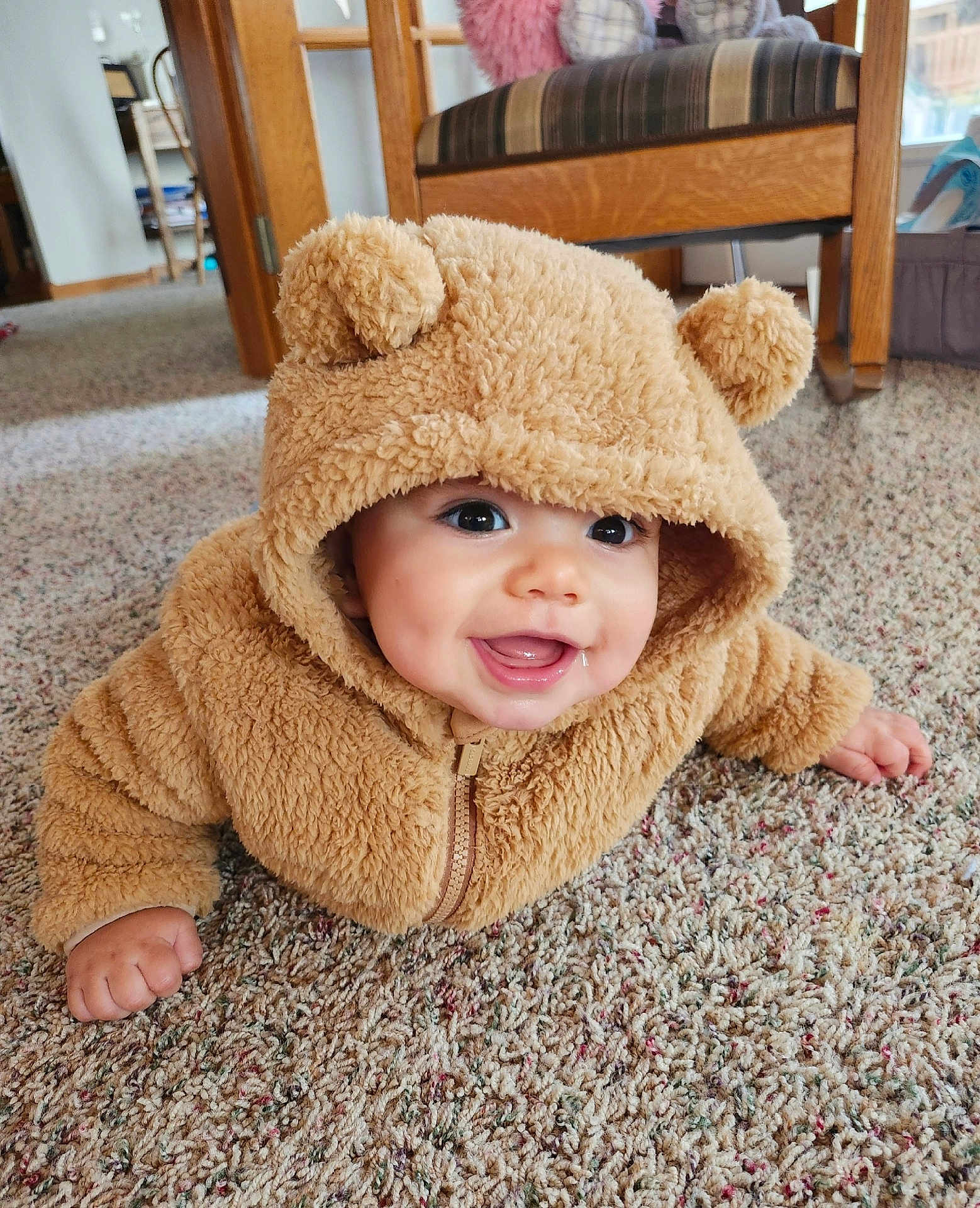 Liam is registered to the contest to win money with this photo: baby, infant, child, teddy_bear_hood, hooded_jacket, fuzzy_coat, carpet, smile, drooling, cute, indoors, portrait, close_up, big_eyes, chubby_cheeks, plush, zipped_jacket, hand, floor, home