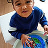 avengers, blue_sweater, child, curly_hair, cute, face, food, hand, indoor, person, plate, playful, room, slippers, smiling, table, toddler, toy, wood_floor, young