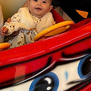 Taylana a rejoint le concours — aidez-le/la à gagner de superbes lots ! baby, child, person, ride, toy_car, red, yellow, white_clothing, fur_vest, cute, smiling, hand, arm, indoor, bright_colors, portrait, happy, head, face, seated
