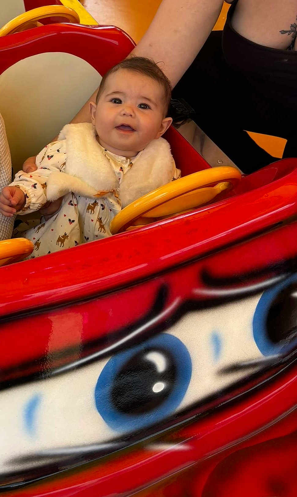 Taylana a rejoint le concours — aidez-le/la à gagner de superbes lots ! baby, child, person, ride, toy_car, red, yellow, white_clothing, fur_vest, cute, smiling, hand, arm, indoor, bright_colors, portrait, happy, head, face, seated