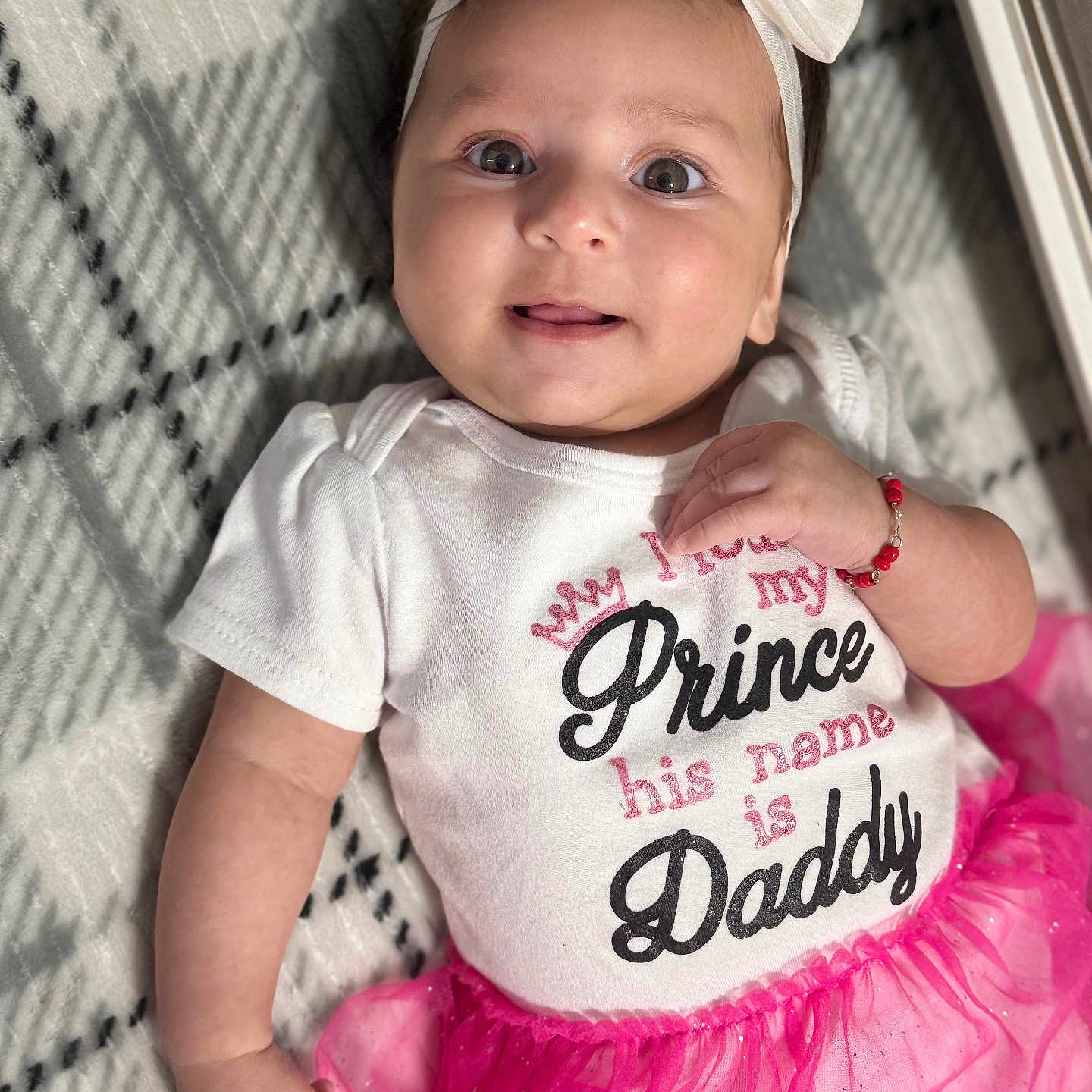Valery is registered to the contest to win money with this photo: arm, baby, blanket, bow, child, cute, face, fashion, hand, happy, headband, indoor, infant, patterned_blanket, person, pink_tutu, portrait, smiling, white_clothing, young_child
