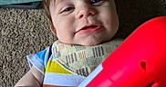 Aidan joined the competition — help win amazing prizes! baby, background, bib, carpet, child, closeup, colorful_clothing, face, hand, happy, indoor, infant, person, playful, playtime, red_toy, smile, soft_lighting, striped_shirt, toy
