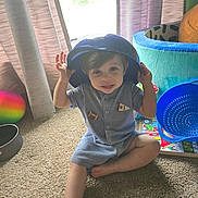 Aidan is registered to the contest to win money with this photo: baby, blue_hat, carpet, child, colorful, curtains, happy, hat, indoors, jumpsuit, photography, playful, playroom, portrait, sitting, smiling, striped_clothing, toddler, toys, window