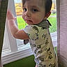 toddler, child, baby, onesie, animal_print, sloth, window, curtains, indoor, green_wall, carpet, natural_light, standing, looking_back, cute, portrait, face, hair, skin, hand
