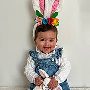 Giolia participe au concours pour gagner de l'argent avec cette photo : baby, child, bunny_ears, headband, plush_toy, soft_toy, denim_overalls, white_blouse, smiling, happy, cute, indoor, portrait, sitting, toy, colorful_flowers, face, hands, young_child, easter_theme