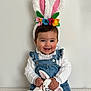 baby, child, bunny_ears, headband, plush_toy, soft_toy, denim_overalls, white_blouse, smiling, happy, cute, indoor, portrait, sitting, toy, colorful_flowers, face, hands, young_child, easter_theme
