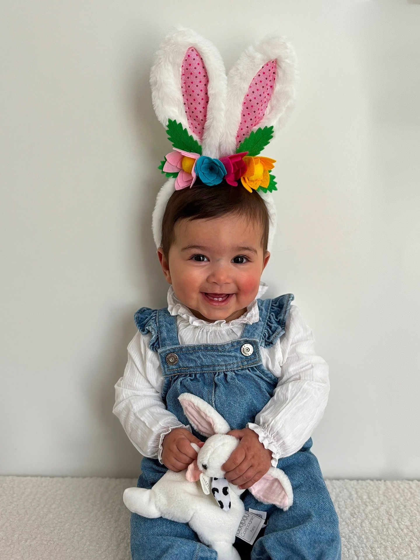 Giolia participe au concours pour gagner de l'argent avec cette photo : baby, child, bunny_ears, headband, plush_toy, soft_toy, denim_overalls, white_blouse, smiling, happy, cute, indoor, portrait, sitting, toy, colorful_flowers, face, hands, young_child, easter_theme