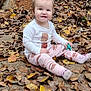 autumn_leaves, baby, casual, child, cute, daylight, fall, ground, happy, leaf_litter, nature, outdoor, pajamas, person, playful, seasonal, sitting, smiling, toddler, toy