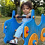 blue, child, curly_hair, cute, daylight, grass, nature, orange, outdoor, park, play, playground, rocker, sandals, summer, toddler, toy, tree, white_clothing, young_child