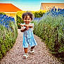 Leyana a rejoint le concours — aidez-le/la à gagner de superbes lots ! blue_dress, child, curly_hair, daylight, flowers, gravel_path, greenery, happy, hedge, house, lavender, nature, outdoor, person, portrait, sandals, smiling, summer, toddler, walking