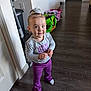 toddler, child, smiling, standing, indoor, floor, purple_pants, grey_shirt, hair_tie, wooden_floor, home, bags, playful, cute, person, clothing, young_child, happy, casual, portrait