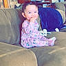 Nevaeh is registered to the contest to win money with this photo: baby, child, pink_pajamas, couch, sofa, living_room, furniture, smiling, happy, indoors, person, home, wooden_cabinet, blanket, comfort, cute, seated, hand_in_mouth, cozy, casual