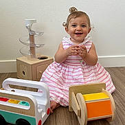 Ghevorchean Suzanna joined the competition — help win amazing prizes! baby, child, smiling, pink_dress, striped_dress, wooden_floor, toy_bus, wooden_toys, rolling_drum, happy, indoor, floor, curly_hair, playtime, cute, sitting, white_wall, person, infant, young_child