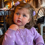 Naya is registered to the contest to win money with this photo: child, toddler, girl, portrait, face, smiling, looking_at_camera, curly_hair, hair_bows, flower_clips, lavender_sweater, polka_dots, earrings, sitting, restaurant, cafe, chair, indoor, warm_lighting, photography