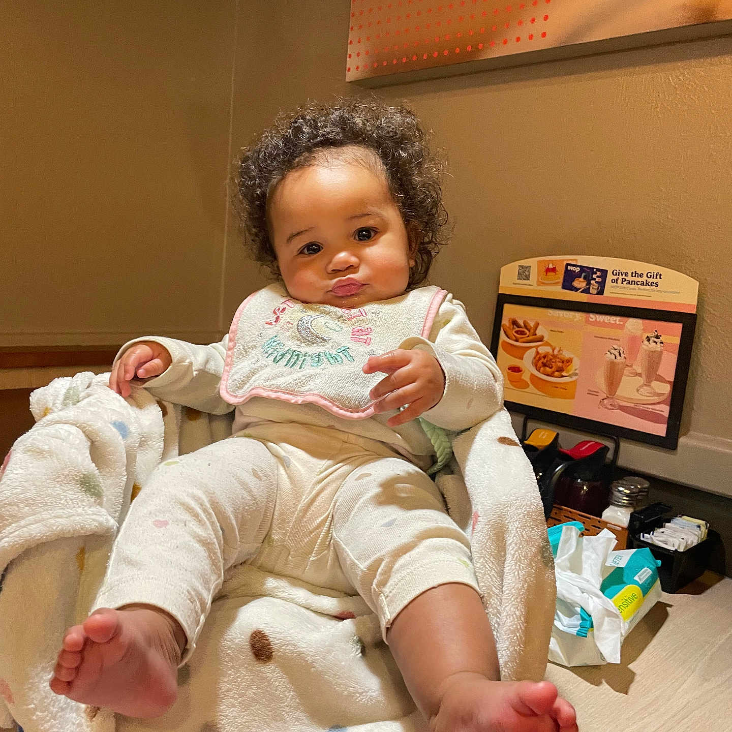 Cyenna joined the competition — help win amazing prizes! baby, child, curly_hair, blanket, bib, pajamas, foot, indoor, chair, table, menu, condiments, wall, room, cute, expression, person, infant, soft, cozy