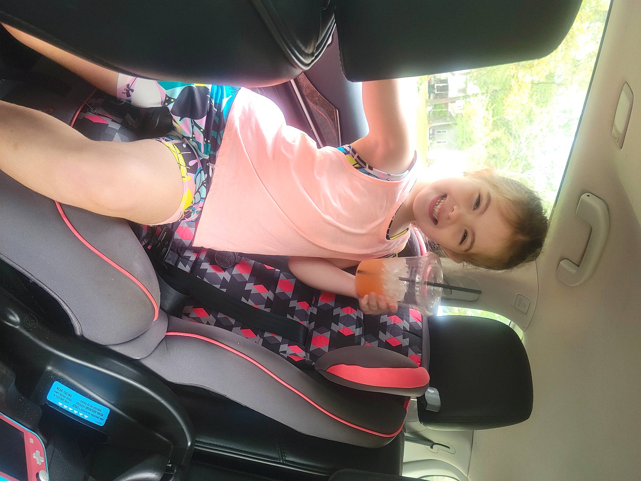 Riley is registered to the contest to win money with this photo: automotive_design, automotive_exterior, automotive_lighting, automotive_tire, automotive_wheel_system, bumper, car, dress, hood, joy, land_vehicle, leg, mode_of_transport, motor_vehicle, person, personal_luxury_car, pink, smile, steering_wheel, thigh