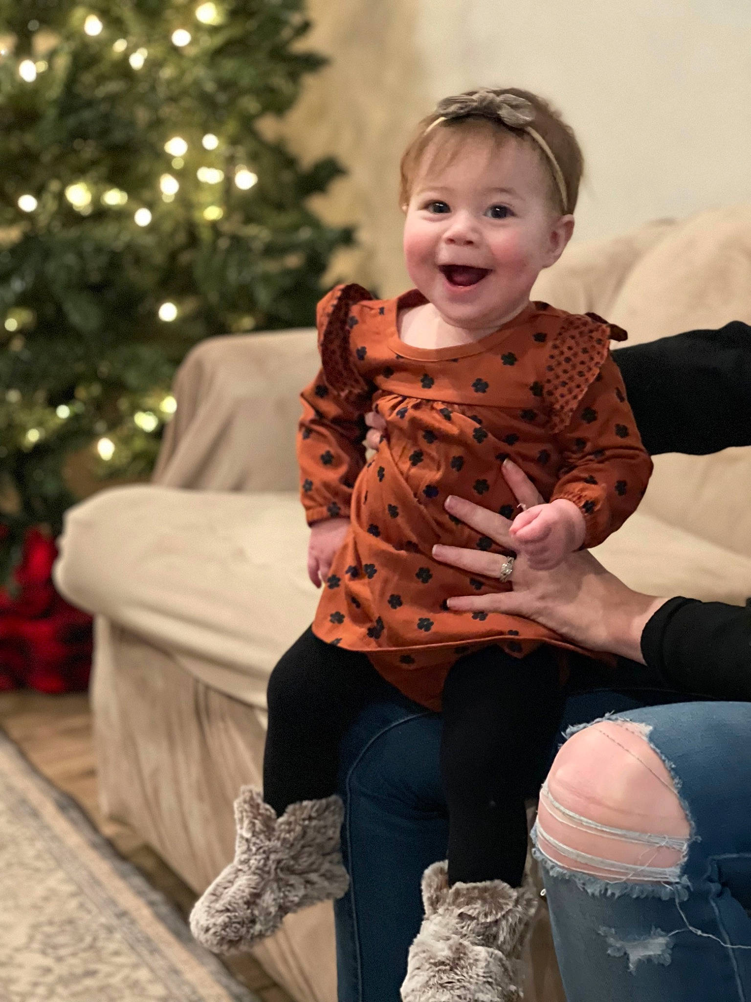 Leilani is registered to the contest to win money with this photo: baby, baby_toddler_clothing, blond, boot, child, christmas_decoration, christmas_tree, event, face, fun, happy, holiday, human_leg, joy, leggings, person, sitting, sleeve, smile, thigh