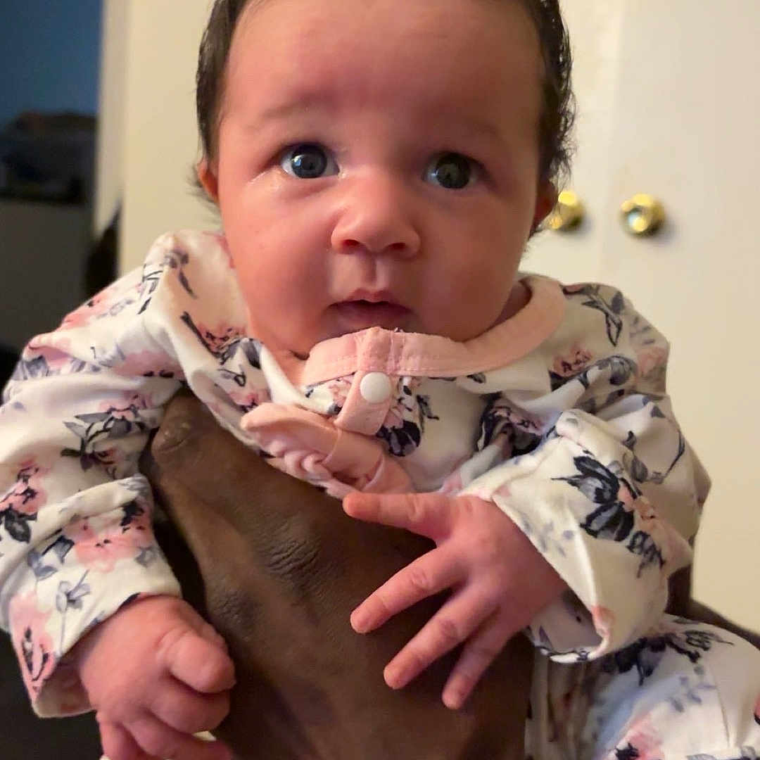 Kenna joined the competition — help win amazing prizes! baby, infant, hand, person, face, clothing, pajamas, indoor, cute, expression, skin, fingertips, holding, young_child, portrait, newborn, curious, eyes, sleeves, door